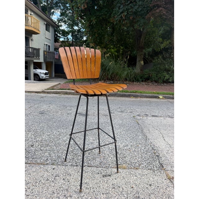 Mid century Arthur Umanoff style bar stool. The stool features Umanoff’s classic wood slats and wrought iron frame. The...