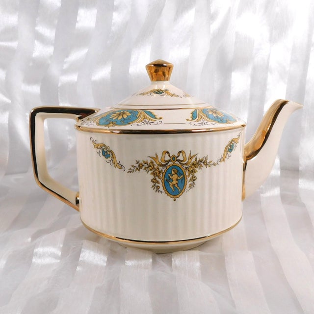 This isa cream Sadler teapot with a ridged design and blue and yellow floral details with cupids on it. It is pattern...