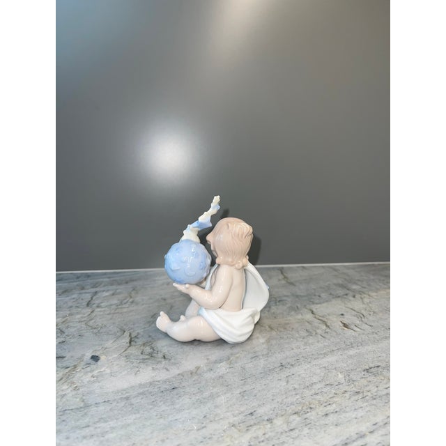 This beautifully crafted piece features a cherubic child seated gracefully, wrapped in a soft white drape adorned with...