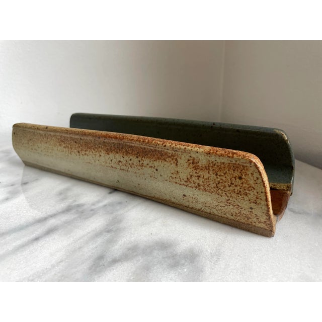 A studio ceramic handmade baguette bread form with a nice overlapping glaze pattern in blue, brown, and natural. Twine...