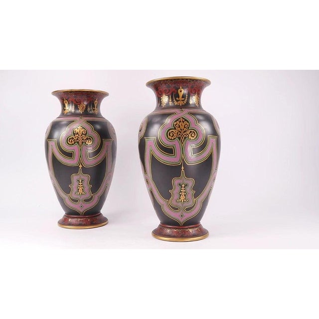 Bold polychrome strapwork ribbons in opaque pink and pale green enamel curve across the body of each vase, standing in...