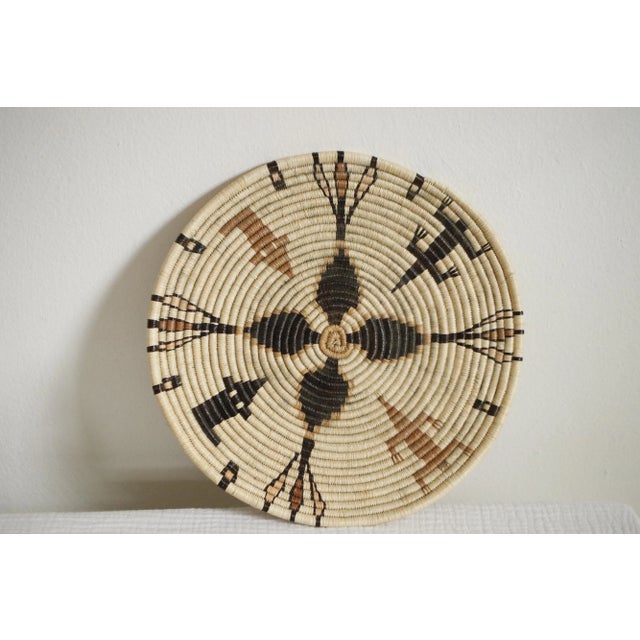 Pictorial coil plaque basket in tones of orange, tan, and black. Handwoven by an unknown weaver. Made from yucca,...