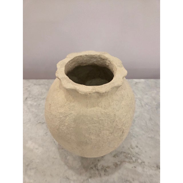A sculptural plaster vase featuring a rounded silhouette, heavily textured surface, and soft cream finish. The organic...