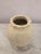 A sculptural plaster vase featuring a rounded silhouette, heavily textured surface, and soft cream finish. The organic...