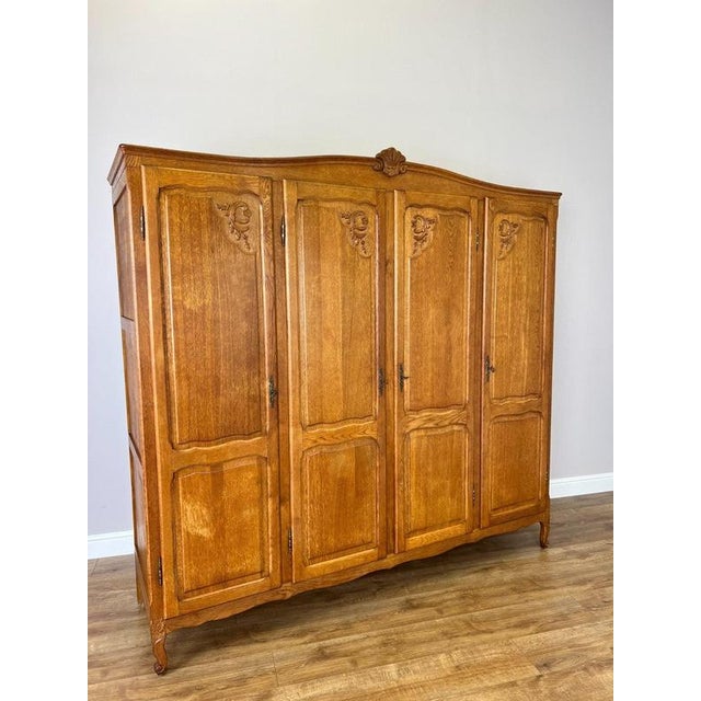 A handsome Vintage French Louis wardrobe in oak, featuring four tall panelled doors with carved decorative motifs, a...