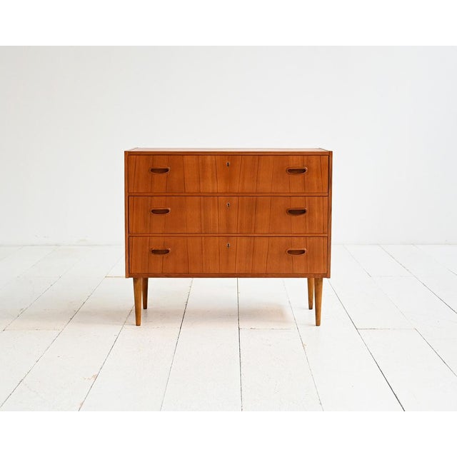Three-drawer teak chest of drawers with carved handles and tapered legs. Karlit label inside. Swedish production,...