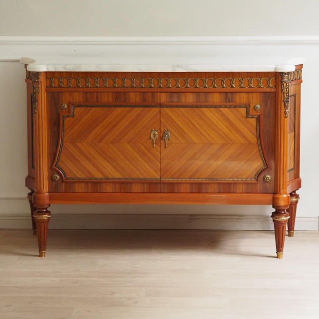 A two-door sideboard in the french louis xvi style, crafted as a high-quality reproduction in solid wood with gilded...