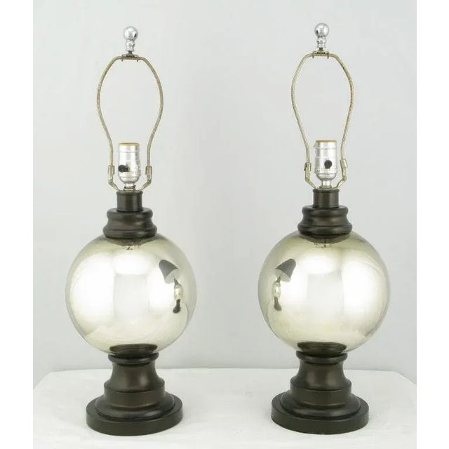 A brilliant pair of mercury glass globe table lamps. The center glass globe is supported by a lacquered resin sculptural...