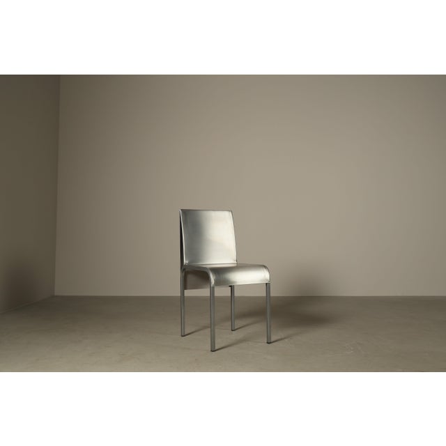 The chairs feature sculptural seats and backs, formed from a single folded sheet of stainless steel, left untreated to...