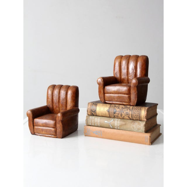 A pair of vintage figural bookends modeled as overstuffed club chairs in a rich brown finish that resembles aged leather....
