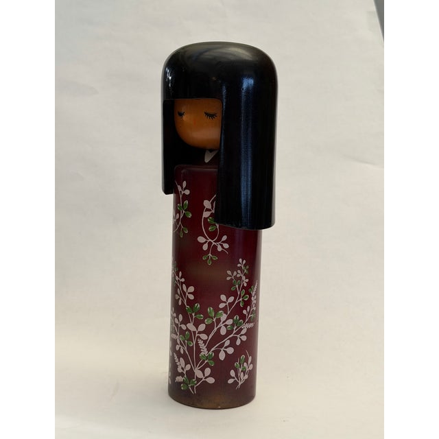 The Doll with a black wig and maroon red kimono with white blossoms and green leaves is a vintage Sosaku Kokeshi doll,...