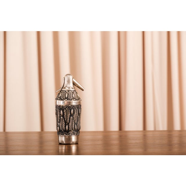 A vintage table cigarette holder in silver-toned metal with repousse floral decoration and brass detailing — a small...