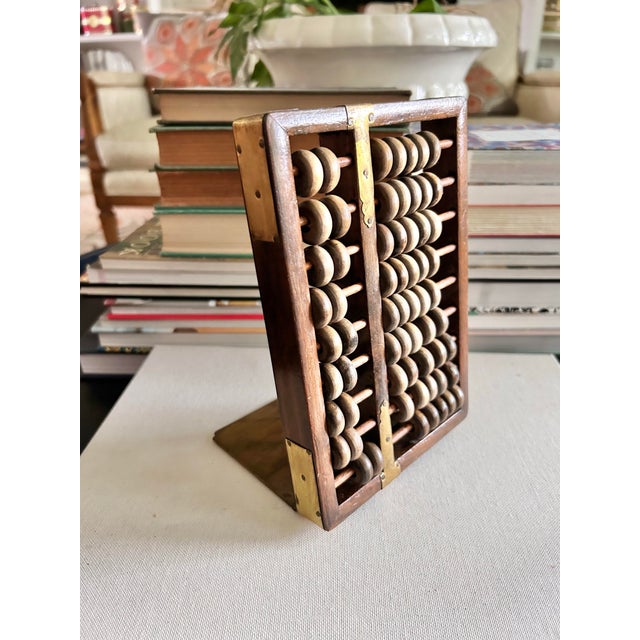 A distinctive vintage abacus bookend crafted from warm-toned wood with aged brass accents and movable wooden counting...