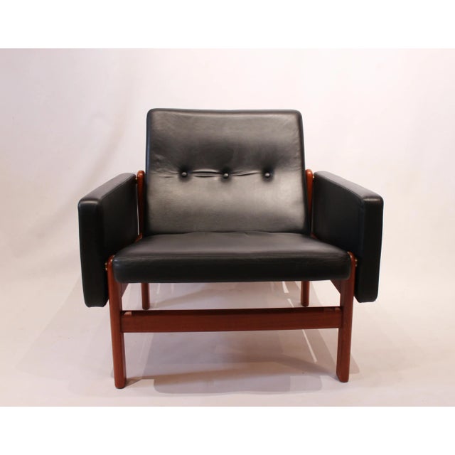 This , model 65 23 easy chair, with model 64 23 stool, is upholstered in black classic leather with a frame in teak. The...
