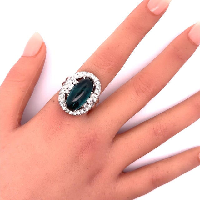 A striking blue tourmaline, weighing approximately 12 carats is the focal point of this contemporary ring. The cabochon-...