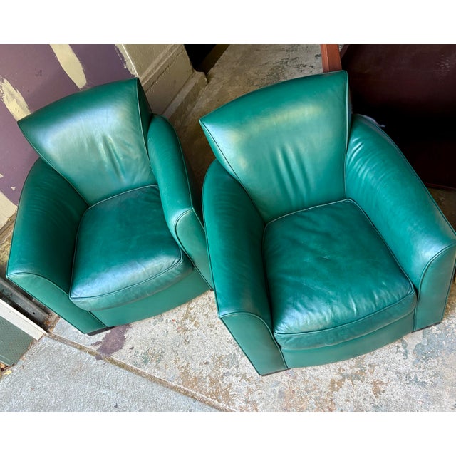 Green leather club chairs with a curved Art Deco silhouette. Each chair has a deep seat cushion, flared backrest, and dark...