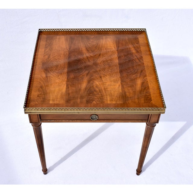 A refined vintage Baker Furniture Louis XVI-style table, exquisitely crafted in book-matched walnut, single drawer with...