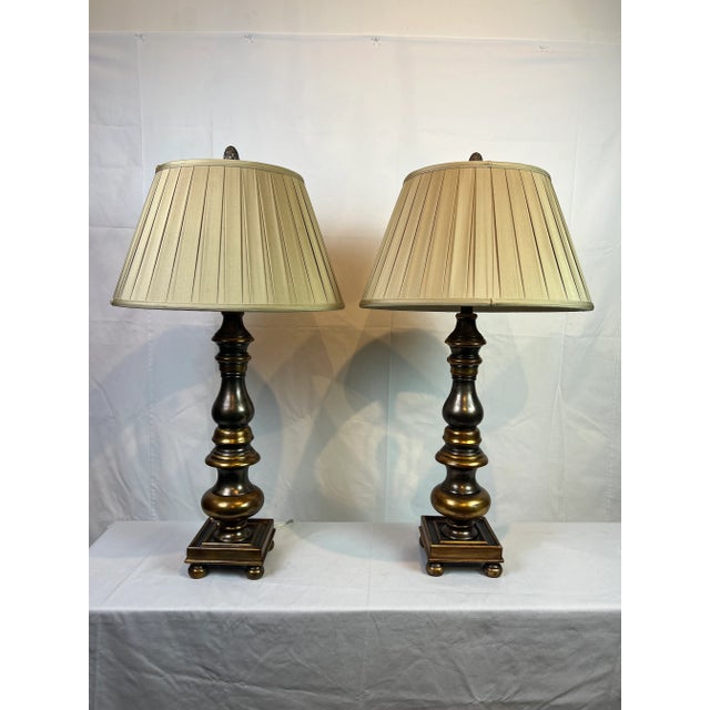 Pair of wooden candlestick style lamp featuring an aged gold finish, square footed base and 20" silk pleated shade with...