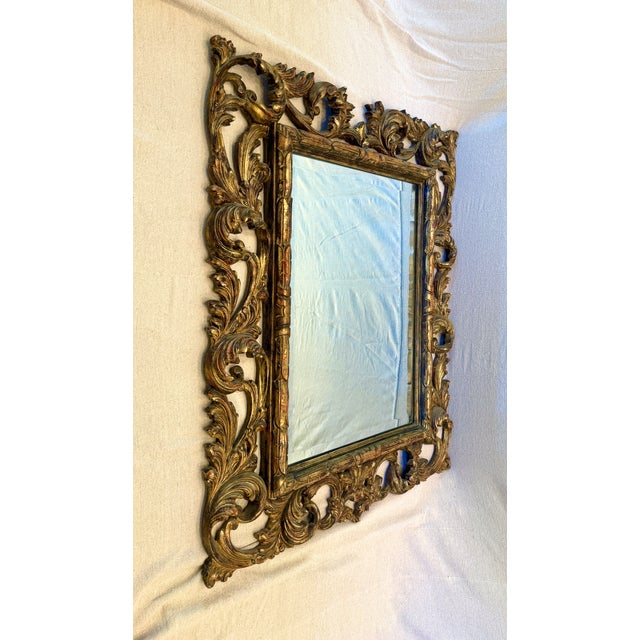 This large Rococo style mirror featuring a carved gilt wood frame with scrollwork decoration has a deeply beveled mirror...