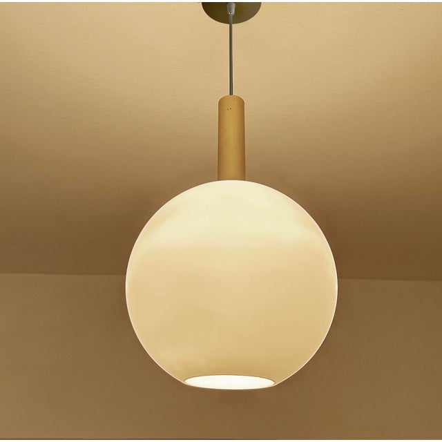 Mid century pendant light featuring a large opaline glass globe shade, brass glass cap, large gold anodized aluminum...