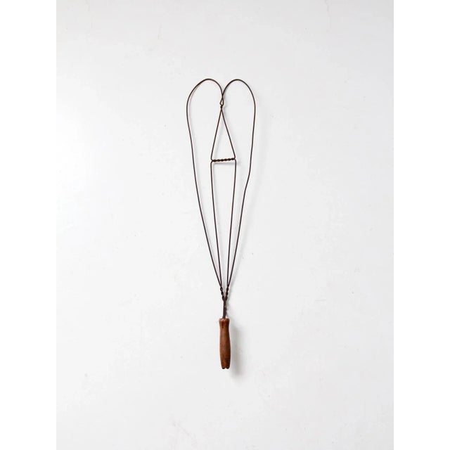 This is an antique rug beater featuring a twisted heart-shaped wire design and a wooden handle. Traditionally used for...