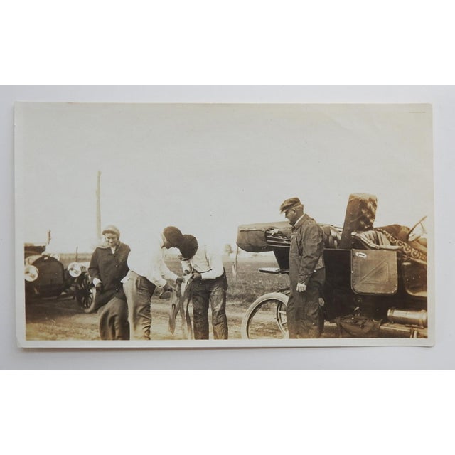 Early 20th century sepia tone snapshot photograph of a road trip tire repair. Two men with onlookers repairing a tire...