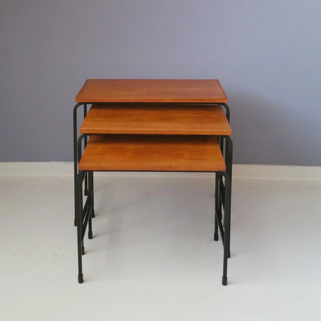 These nesting tables feature teak veneer tops and bar steel legs. The measurements indicated are those of the biggest table.