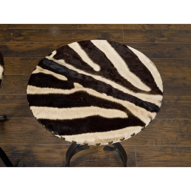 A pair of French iron guéridon side tables from the mid 20th century with round zebra hide tops, twisted bases on three...