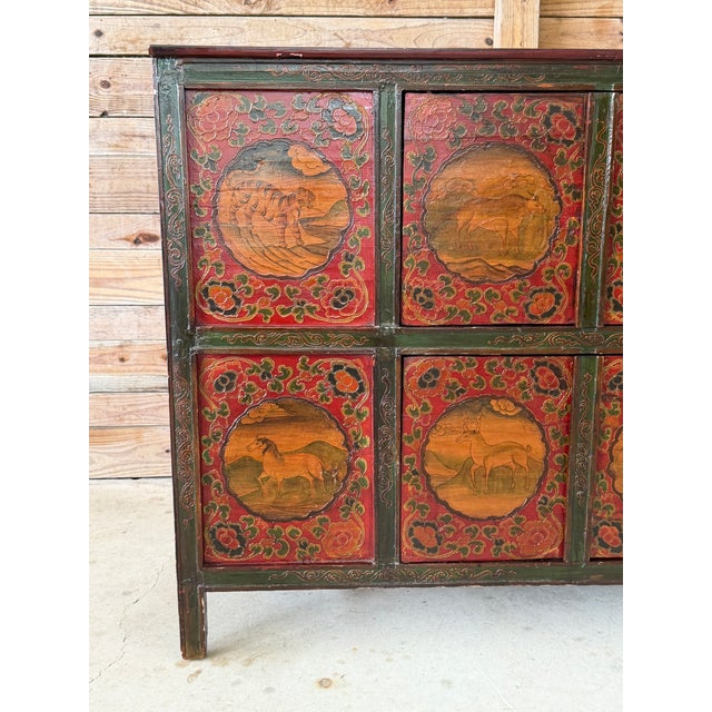 A striking vintage Tibetan polychrome painted cabinet featuring eight individually decorated front panels with hand-...