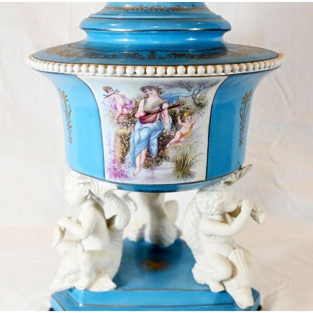 An impressive pair of Sevres-style porcelain covered urns, richly decorated in sky blue, white and gold Each urn has a...