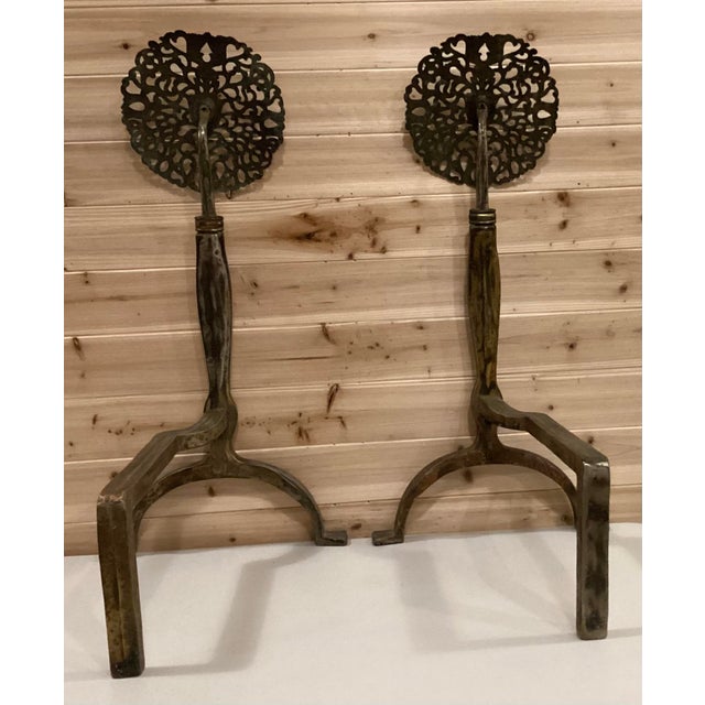 Pair of impressive andirons with large elaborately cast and hand hammered pierced brass rose heads mounted on shaped steel...