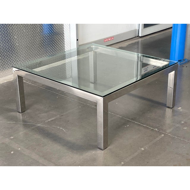 A striking example of modernist design, this square coffee table pairs a thick, inset tempered glass top with a polished...
