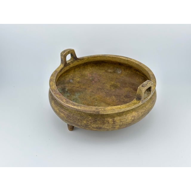 This bronze censer features a classic squat circular form with two loop handles and three peg feet, embodying traditional...