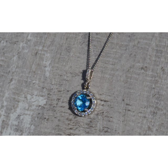 The Elliana Ladies Topaz and Diamond Halo Necklace in 14K. The lush round-cut Swiss blue topaz of this 14k white gold...