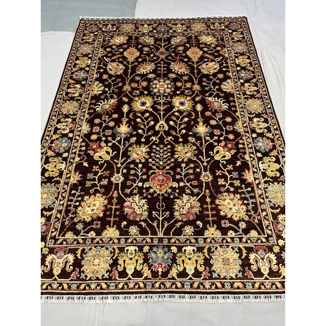 This black and gold Afghan Sultani wool area rug features a Persian-inspired floral design with scrolling vines,...