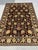 This black and gold Afghan Sultani wool area rug features a Persian-inspired floral design with scrolling vines,...