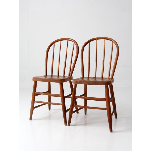 A pair of vintage Windsor bow back chairs in warm wood tones, featuring gently curved crests and classic spindle backs....