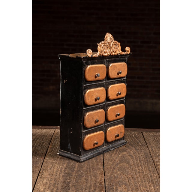 Painted tin spice cabinet featuring eight small drawers arranged in a two-column grid, each fitted with rounded copper-...