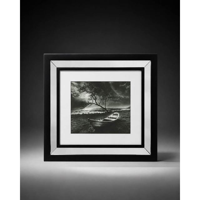 Elegant black and white framed landscape photograph featuring a small boat, tree, shoreline, and dramatic outdoor scenery....