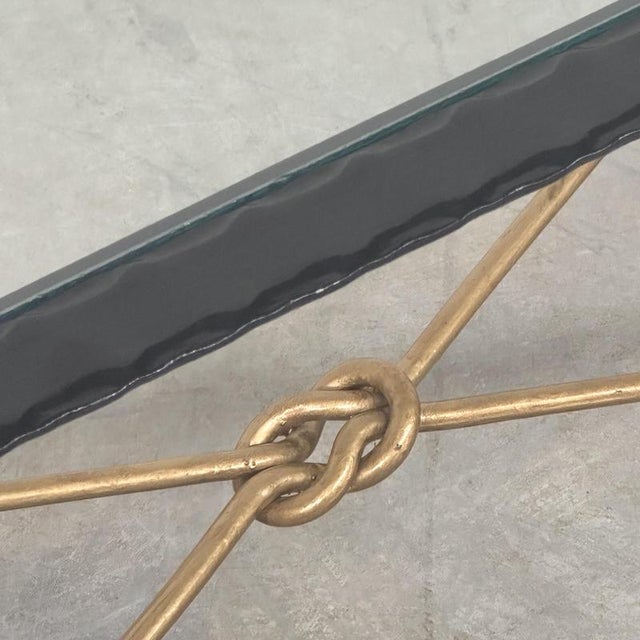 A striking vintage forged iron coffee table combining a sculptural black metal frame with elegant gilt detailing and a...