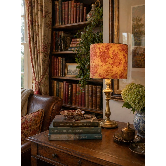 A richly layered vintage brass table lamp paired with a custom rust-toned toile lampshade—an atmospheric piece that brings...