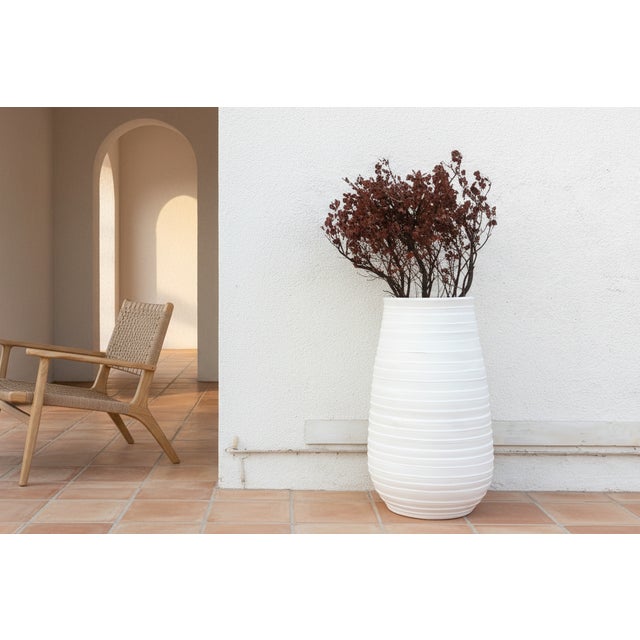 This elegant large terracota vessel emphasizes verticality and texture. Shaped like a tall, slender barrel it stands an...