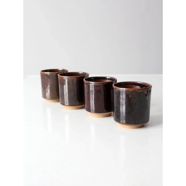 This is a set of four vintage studio pottery cups. The hand-crafted mugs has a dark brown glaze with russet accents.