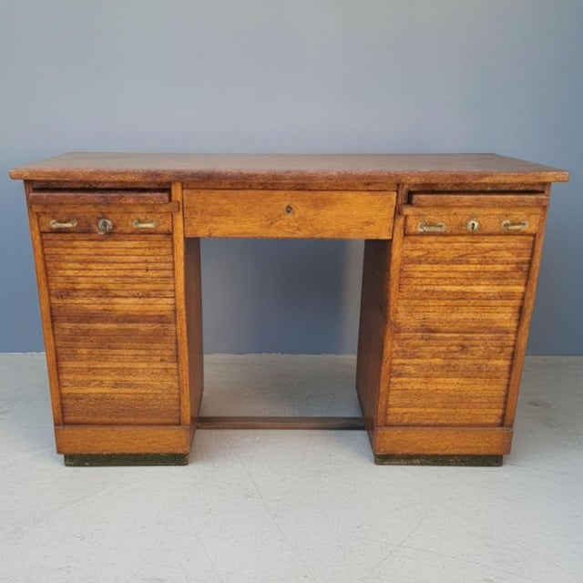 Functional oak roll-front desk from the 1930s, featuring tambour sliding fronts on both pedestal sections and a central...