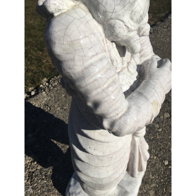 This is a large terra-cotta sculpture with a crackled cream glaze. This large sculpture of an Asian man with very fancy...