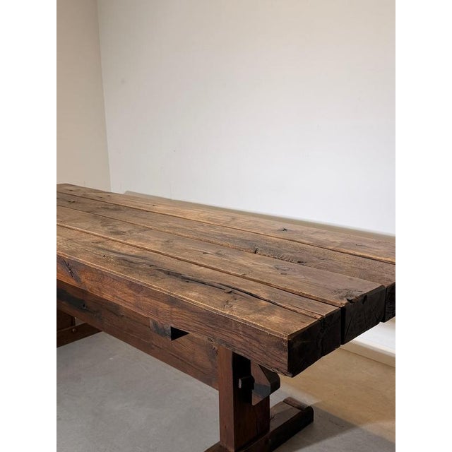 Impressive rustic dining table crafted from solid wood, featuring a substantial plank top and a traditional trestle-style...