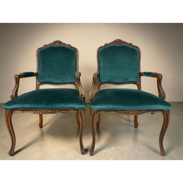 Elegant pair of Louis XV style armchairs featuring beautifully carved walnut frames with floral and grape cluster crest...