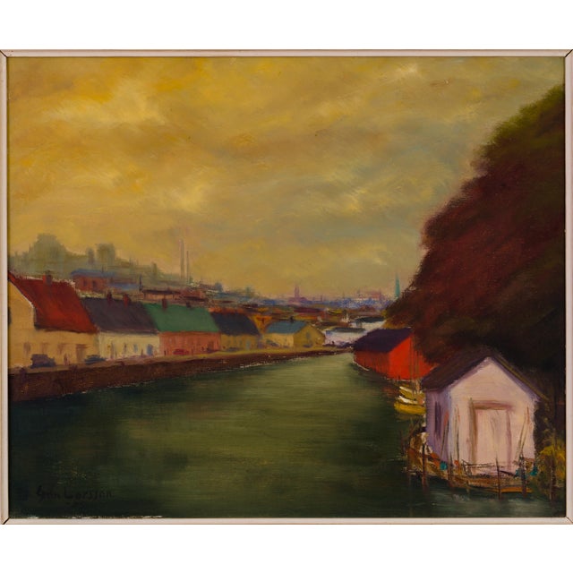 A signed Swedish oil painting by Egon Larsson, dated 1955, depicting a quiet canal or waterfront district beneath a...