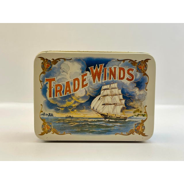 A vintage tin box with a tropical sunset scene with a masted sailing ship in full sail against a backdrop of clouds.