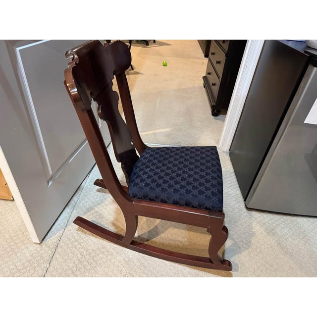 Antique child-size wooden rocking chair with a low profile, upholstered seat, and distinctive vase-form central back splat...
